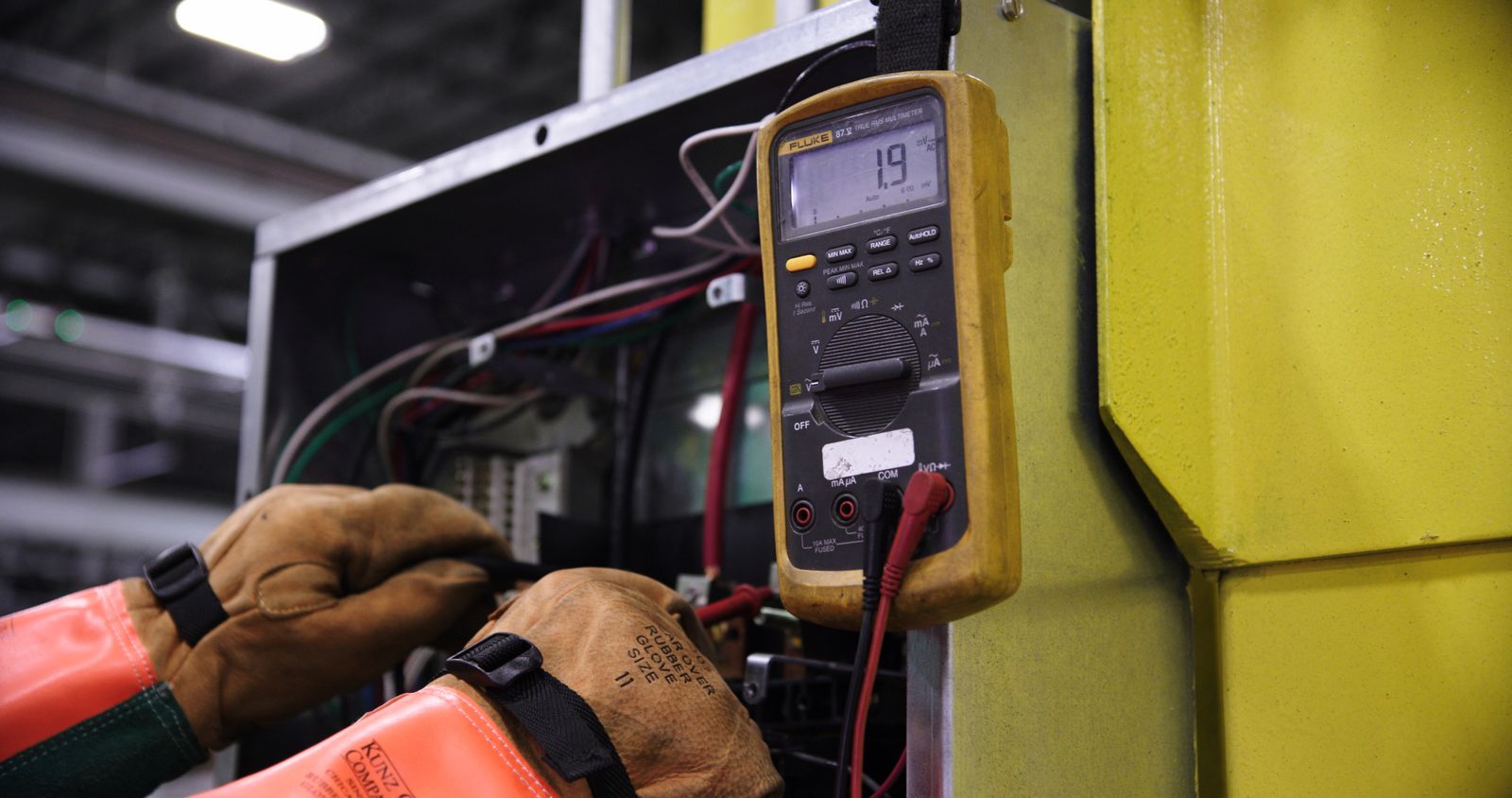 Gloved hands using a multimeter to test electrical equipment