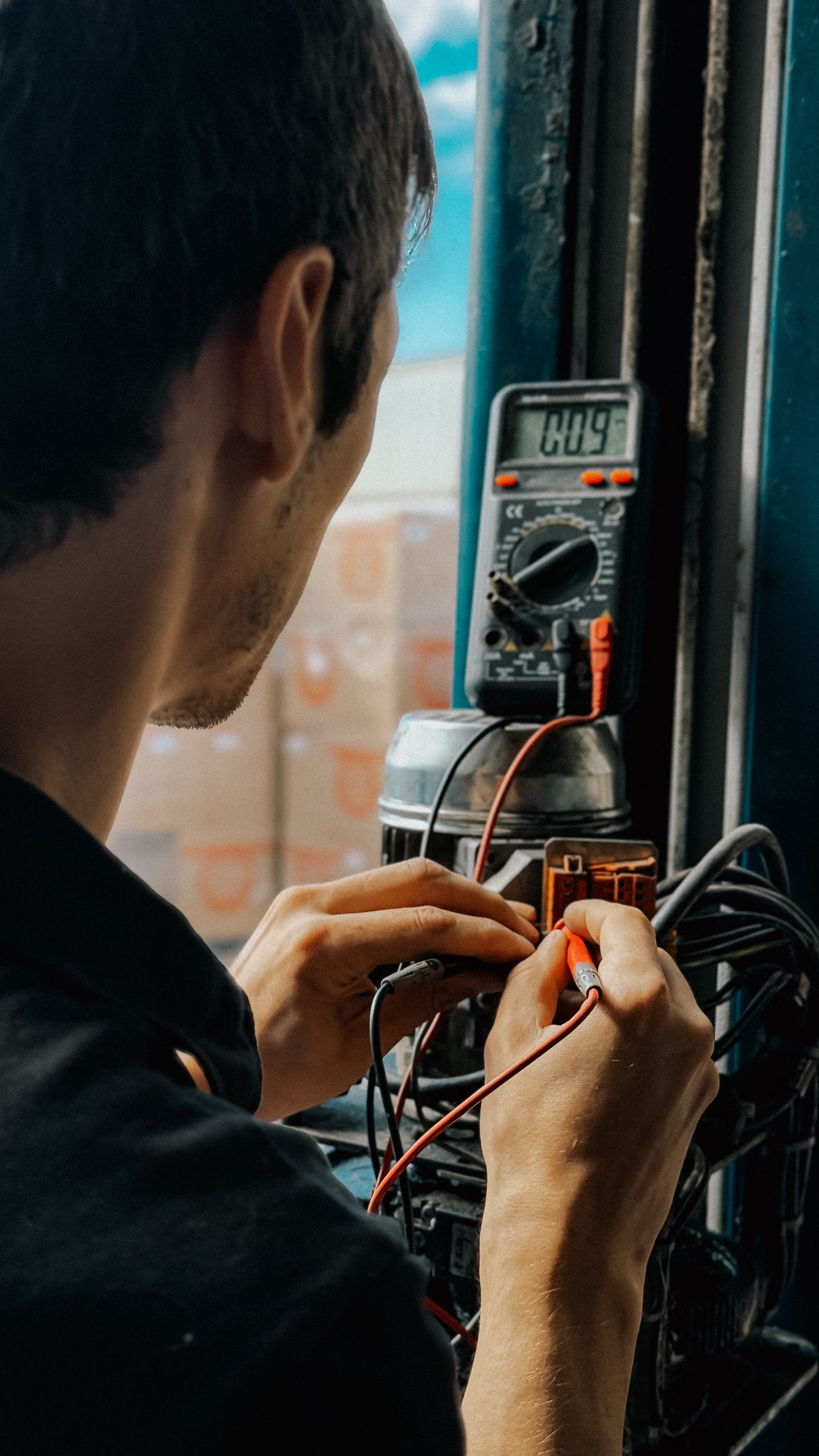 Electrician using multimeter probes at an electrical control cabinet