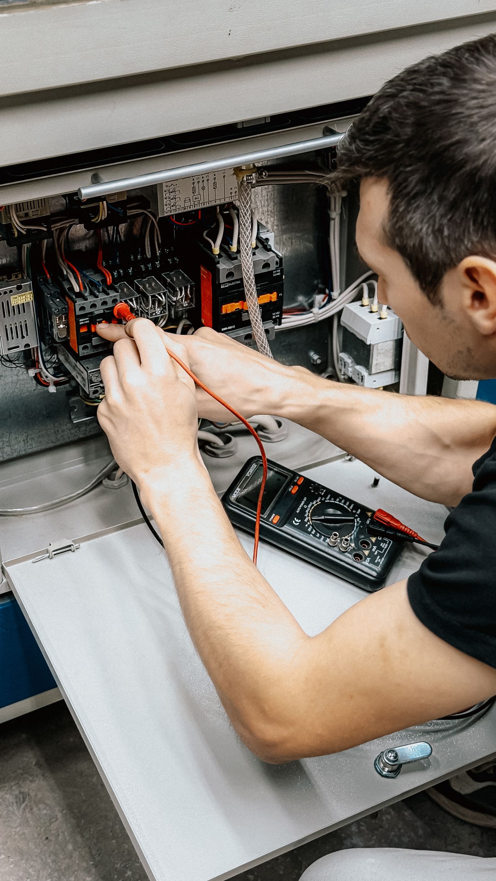 Electrician testing connections inside an electrical panel with a multimeter